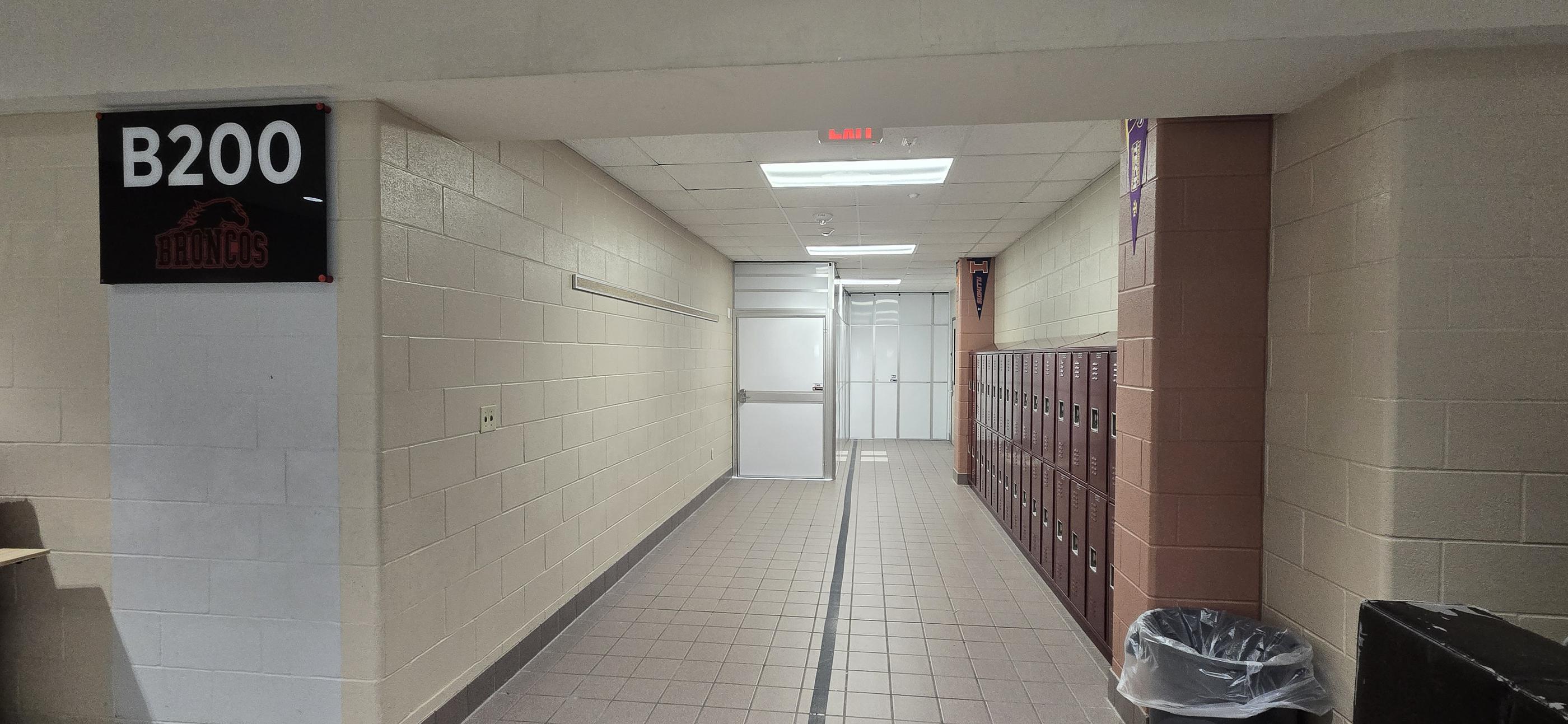 Wide view of secure temporary containment and a push-bar exit door within an occupied middle school corridor.