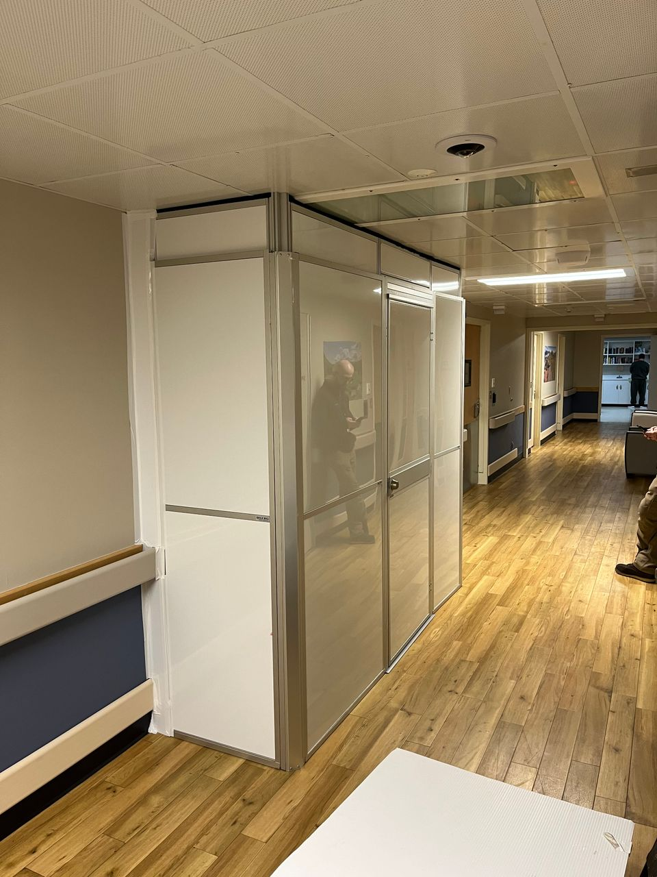 Modular healthcare construction containment with reinforced panels and anti-ligature hardware installed in an occupied behavioral health corridor during phased patient room door replacement.