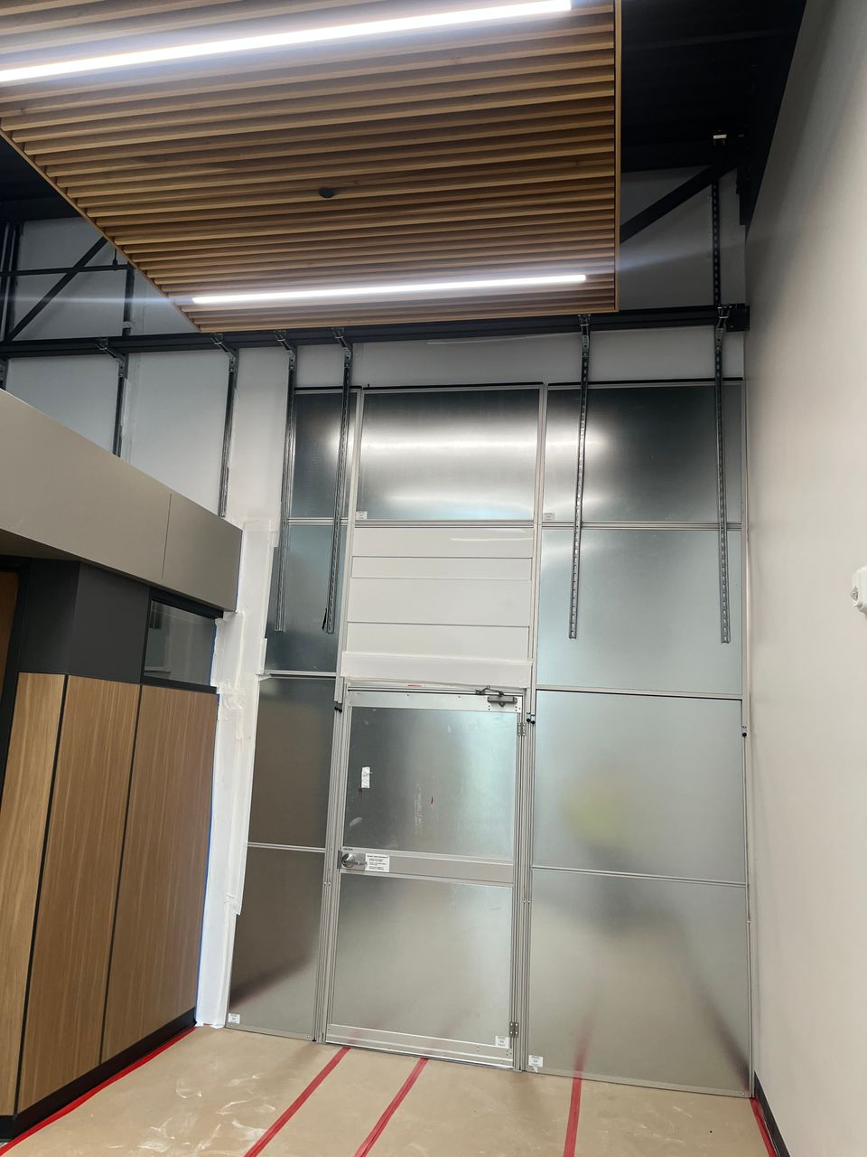Custom floor-to-deck temporary construction wall with a crash-bar emergency exit door separating an active healthcare expansion from occupied clinical spaces.