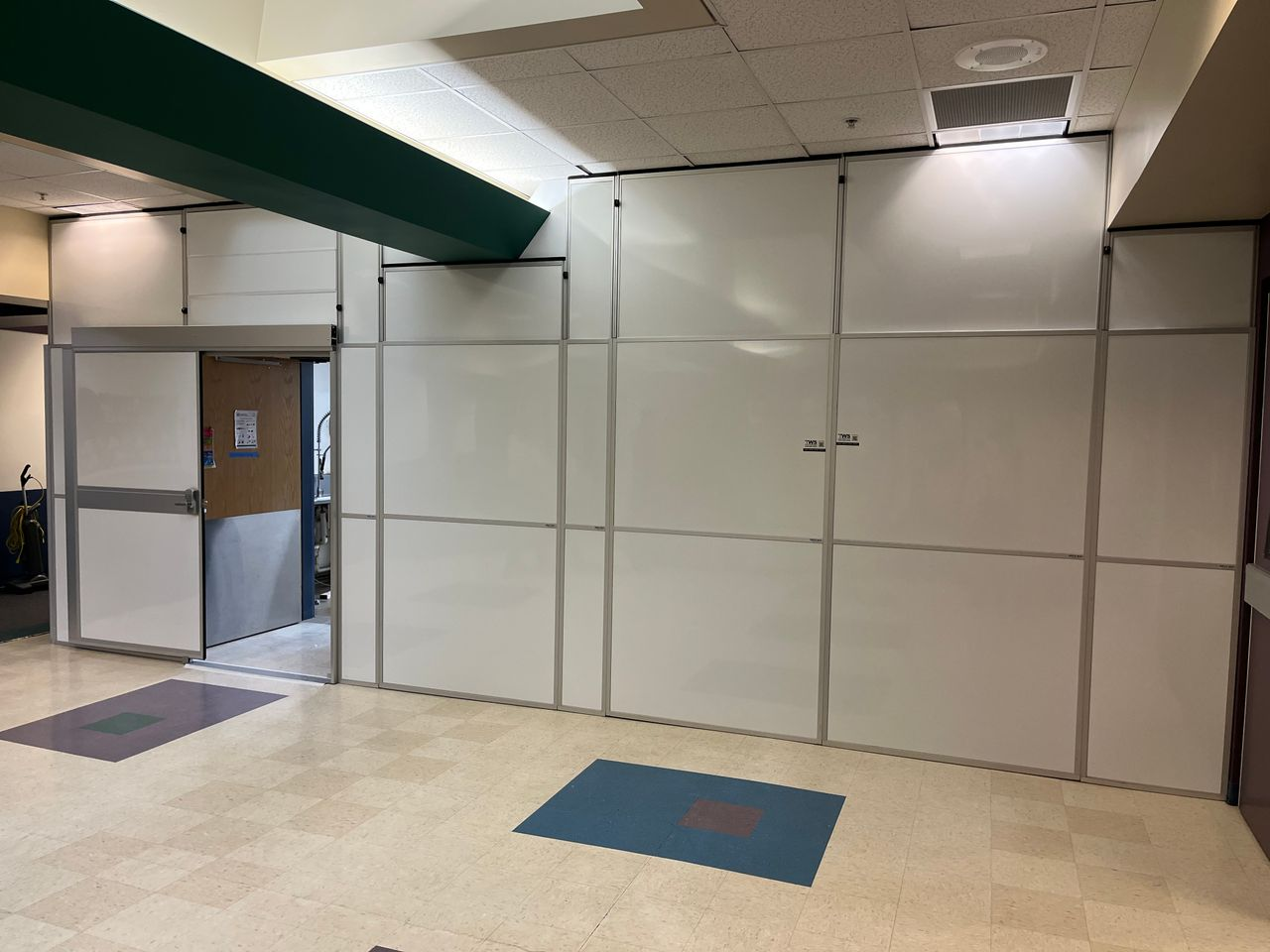Modular hard wall containment installed by Temporary Wall Systems during an elementary school kitchen renovation, featuring secure sliding door access to separate students from the construction area.