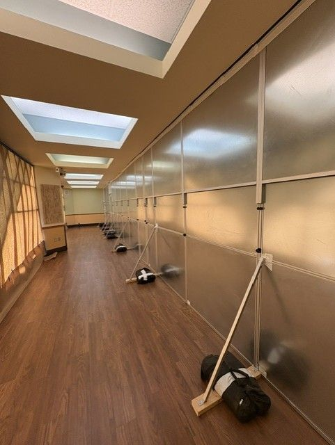 Freestanding modular hard wall containment installed along a hospital cafeteria corridor with corner bracing and ballast supports for healthcare construction containment.