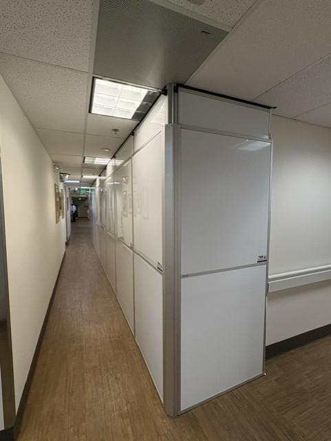 Freestanding temporary containment wall extending through an active cardiology clinic corridor.