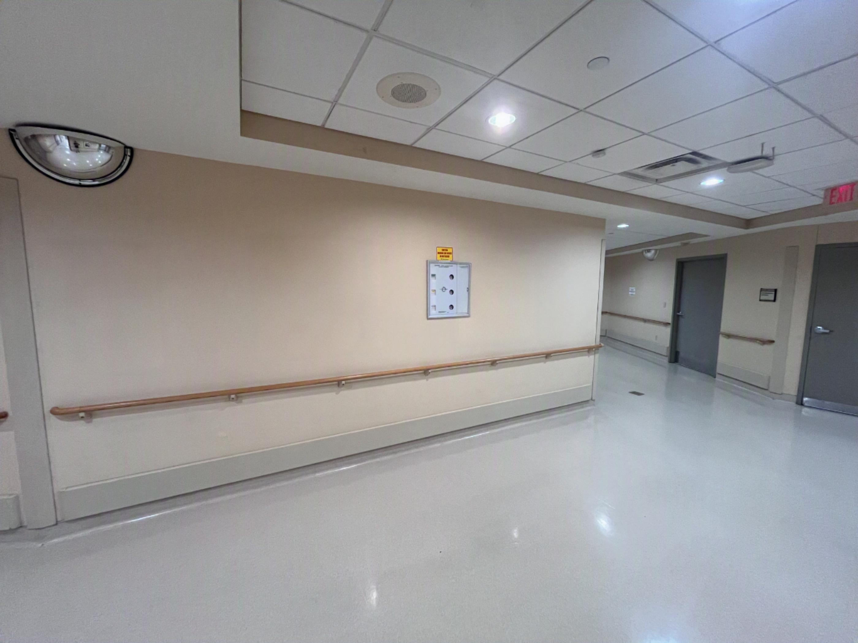 Hospital corridor before installation, showing handrails and a medical gas panel within the future containment area.