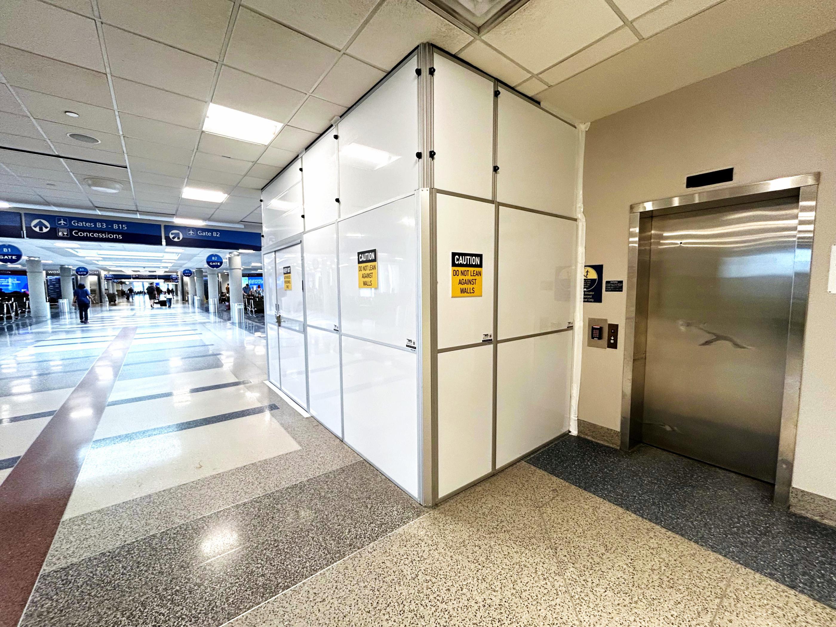 White modular containment wall configured beside an elevator in an active airport concourse.