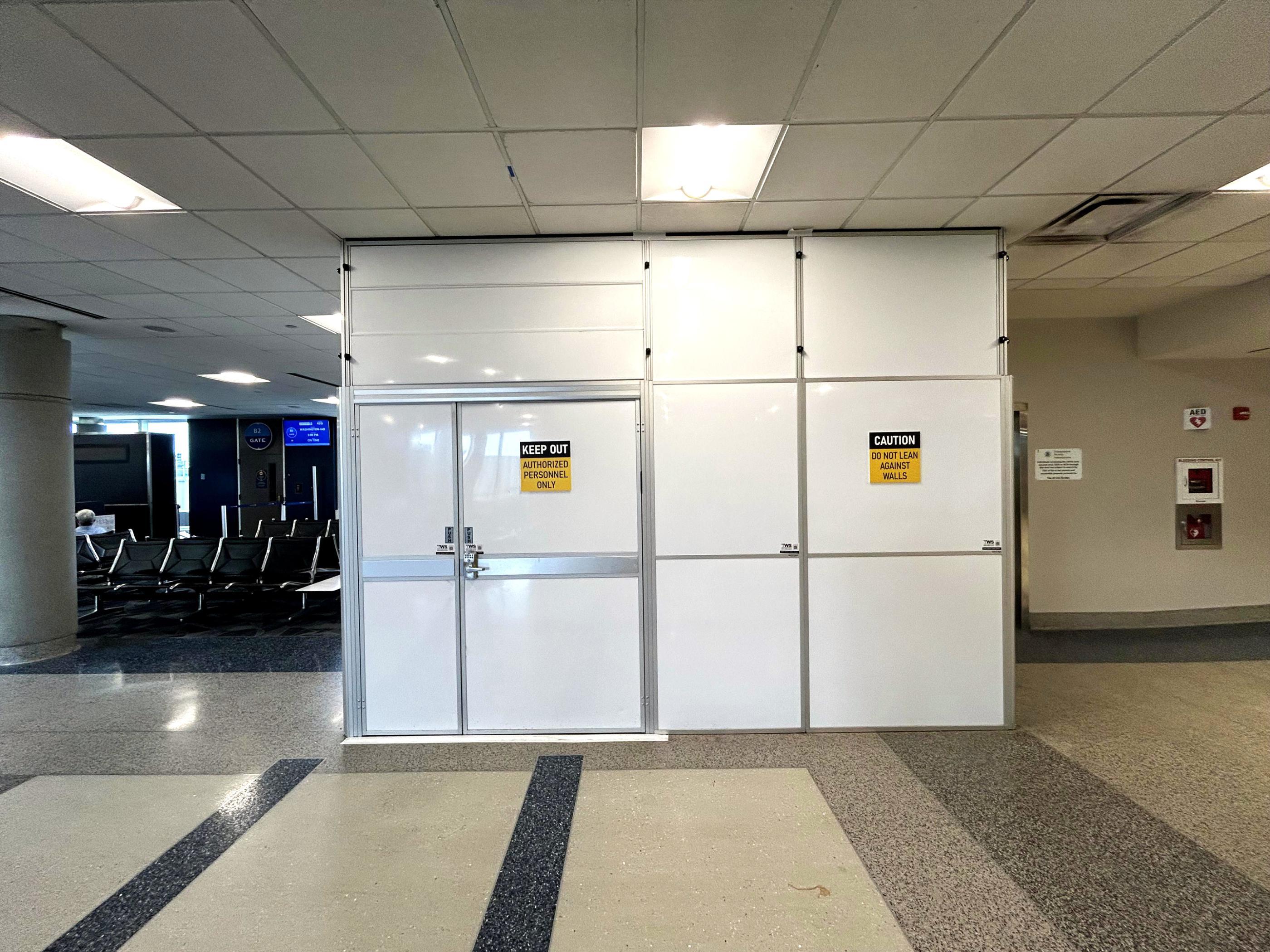 Temporary containment enclosure with double access doors near the Gate B2 seating area at Richmond International Airport.