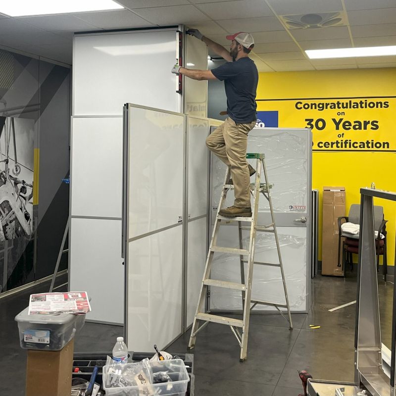 a man on a ladder working on a temporary wall with a yellow wall in the background