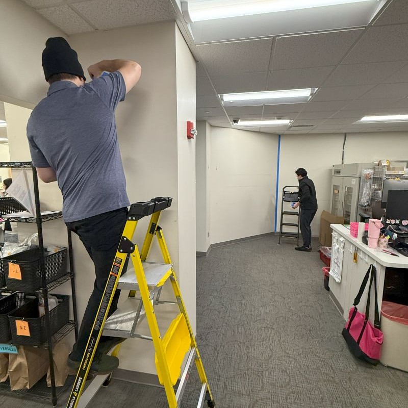 man on a yellow ladder installing brackets for a temporary wall system in a hospital