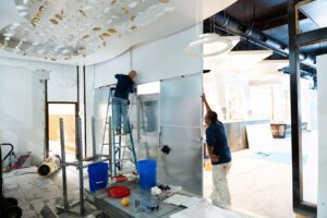 two men working on installing temporary walls. one man is on a ladder the other is holding the wall